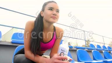 一个<strong>阳光</strong>明媚的日子，年轻的亚洲运动员女孩正坐在<strong>体育</strong>场休息。